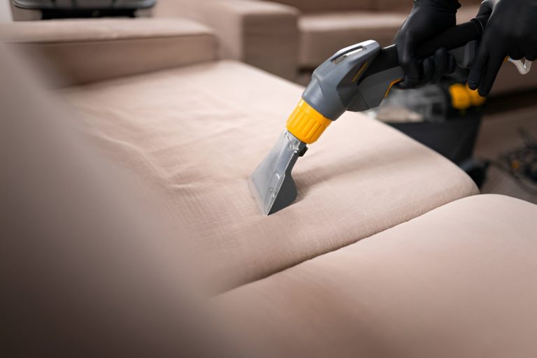 close-up of a hand cleaning an upholstered couch with a vacuum cleaner