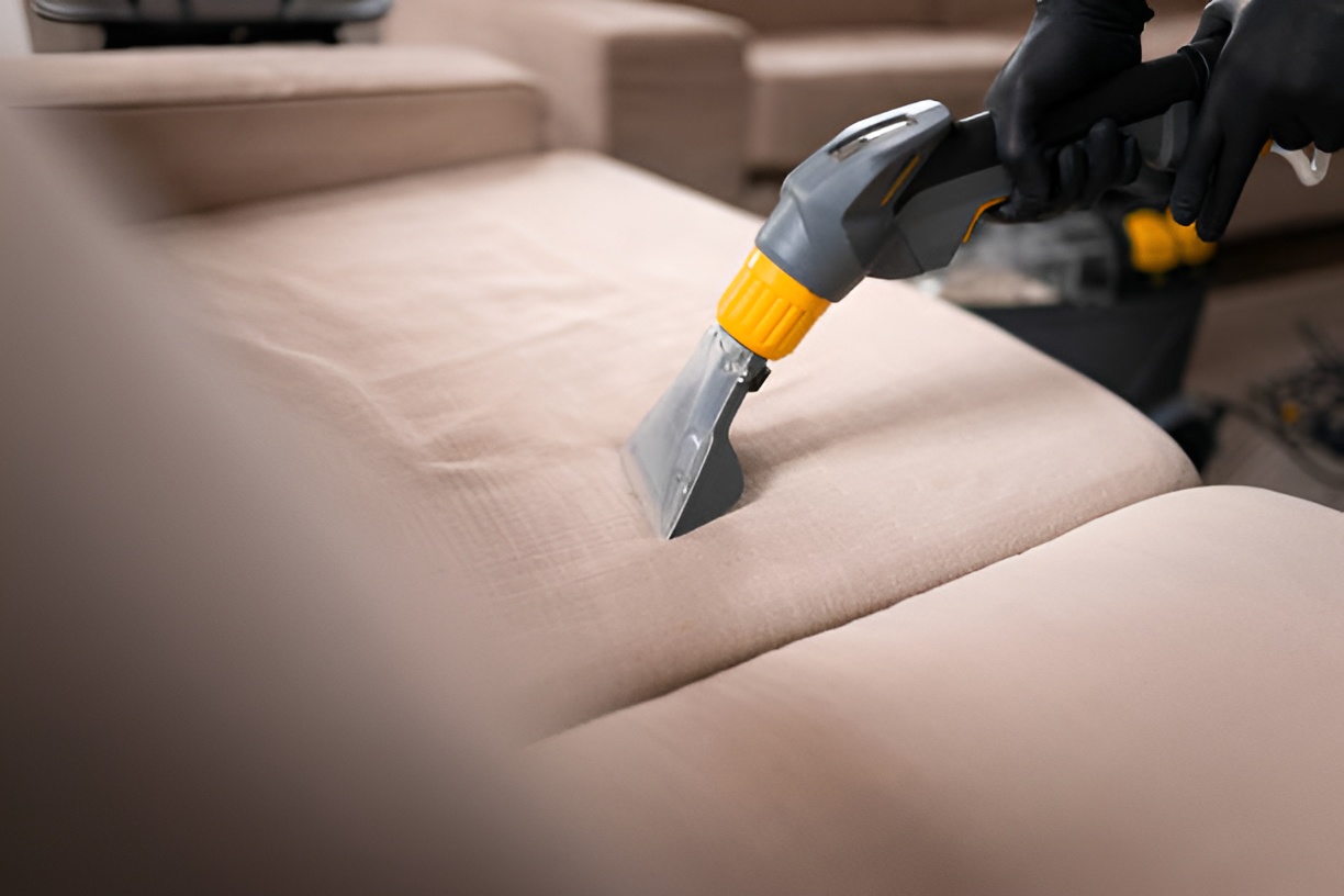 close-up of a hand cleaning an upholstered couch with a vacuum cleaner