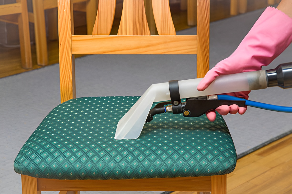 close-up of a gloved hand cleaning an upholstered chair with a vacuum cleaner
